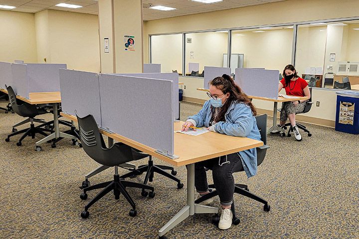 Two students taking tests in the testing center at different desks.
